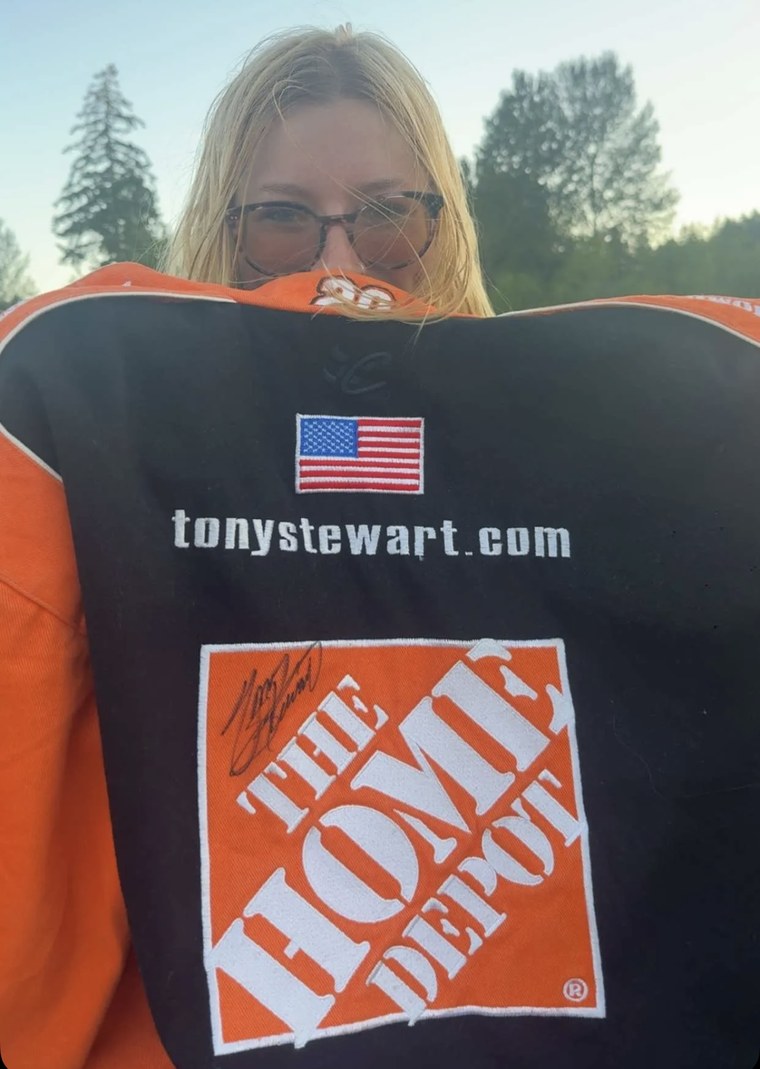 Stasia Smith holding up her Tony Stewart Racing jacket, with Tony Stewart’s signature on the Home Depot panel.